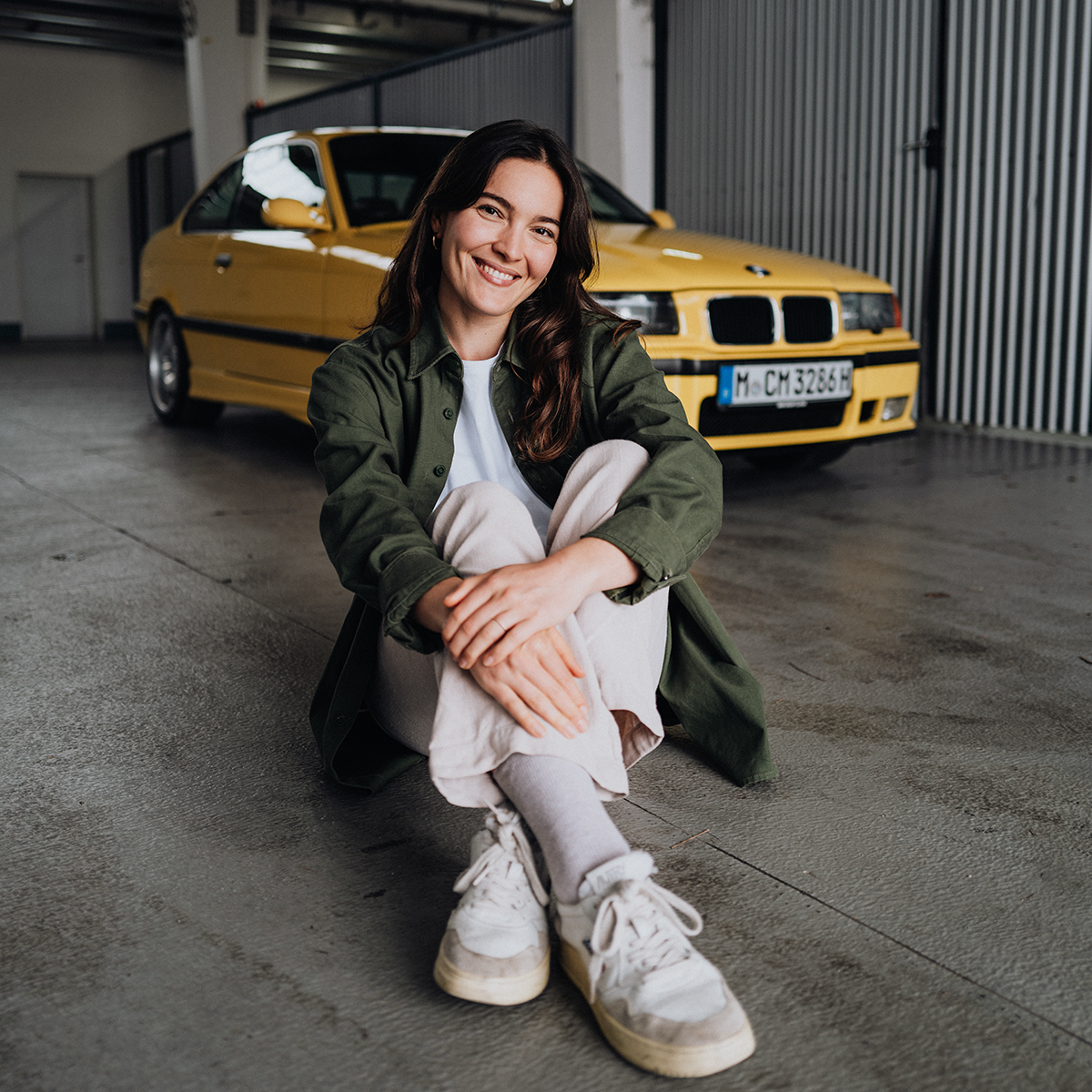Praktikantin Alexia sitzt am Boden vor einem gelben BMW E36 M3
