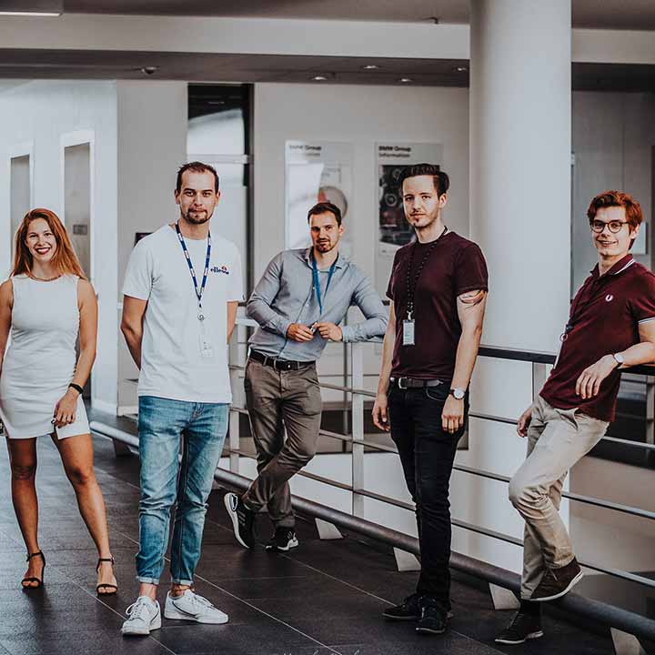 Five students standing in a office environment smiling at the camera.
