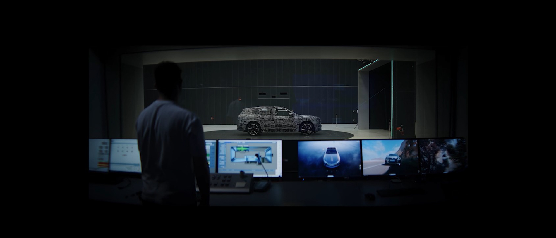 Car rear in a production hall surrounded by multiple industrial robots at assembly lines.