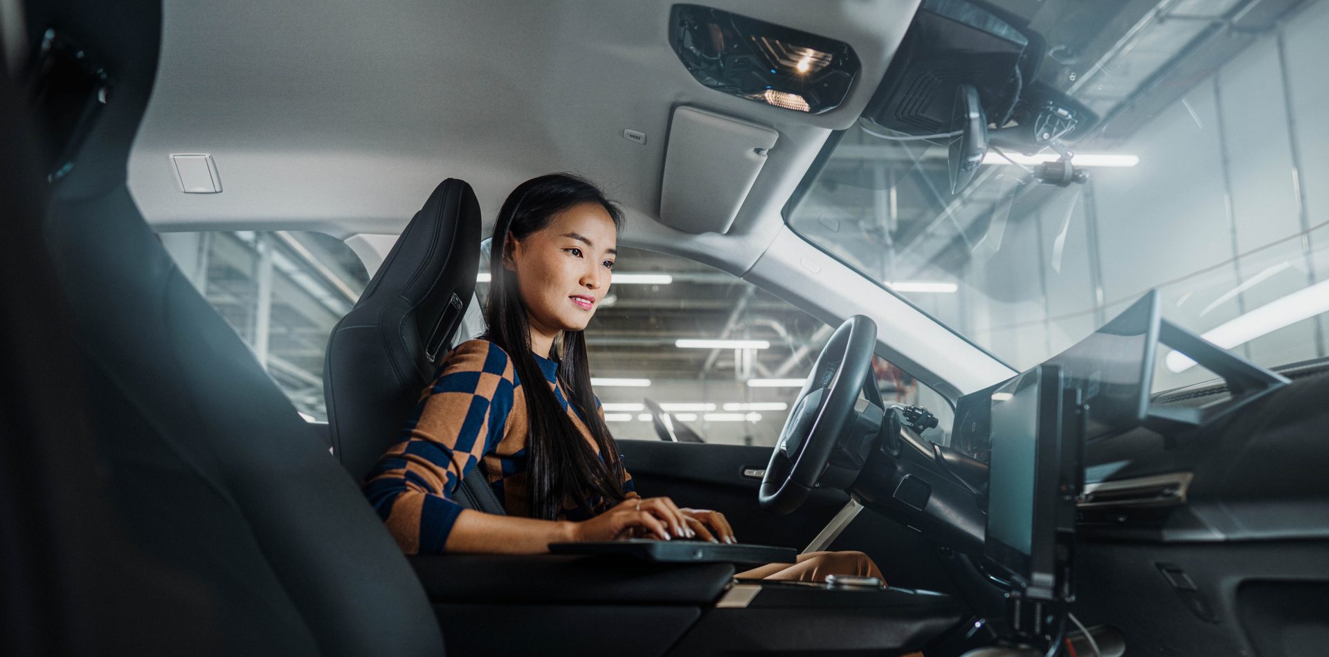 The picture shows a BMW employee working in Software Development checking a car with her laptop.
