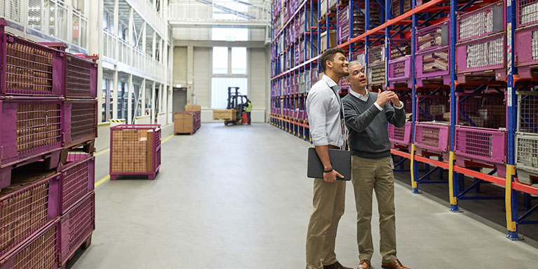 The picture shows two BMW logistics employees talking in a warehouse.	