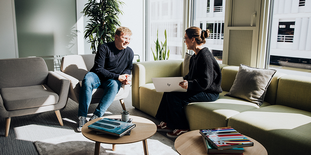 Two colleagues having a chat on sofas in a sunny office
