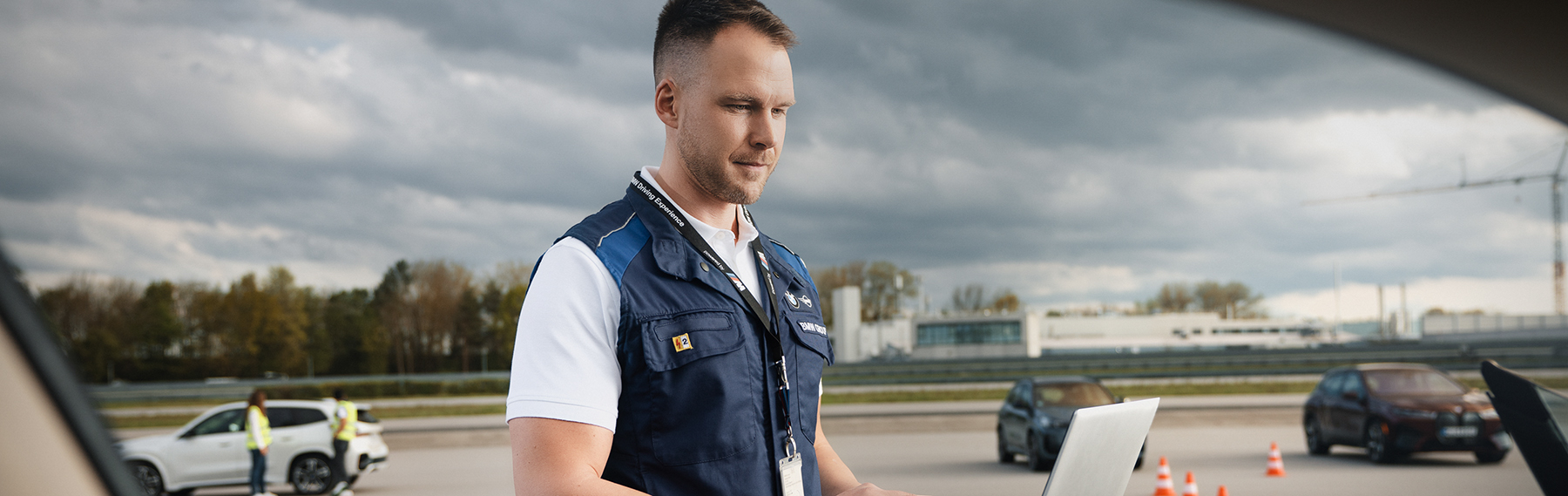 Safety Engineer at the test track looking at his laptop with cars in the background