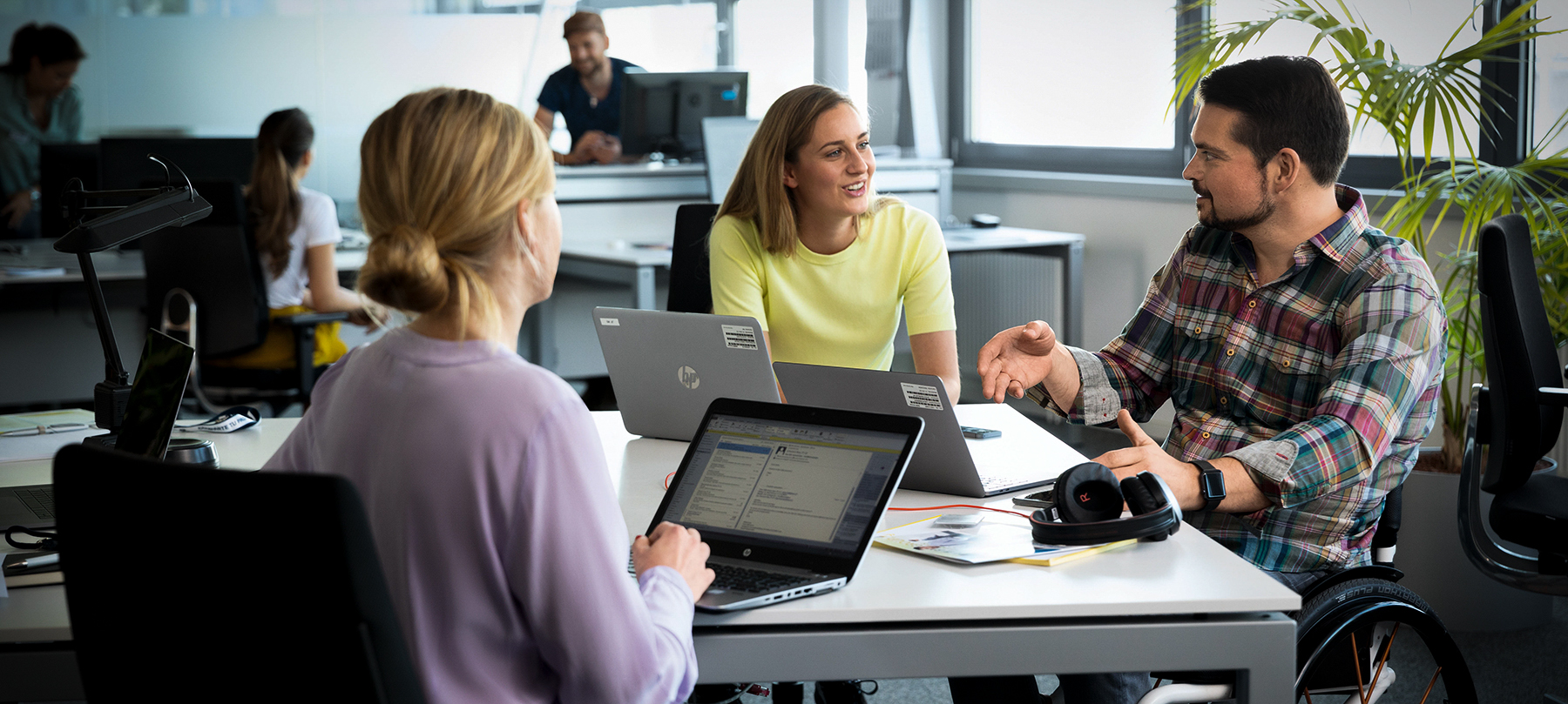 Trois collègues, dont un en fauteuil roulant, travaillant ensemble dans un bureau.