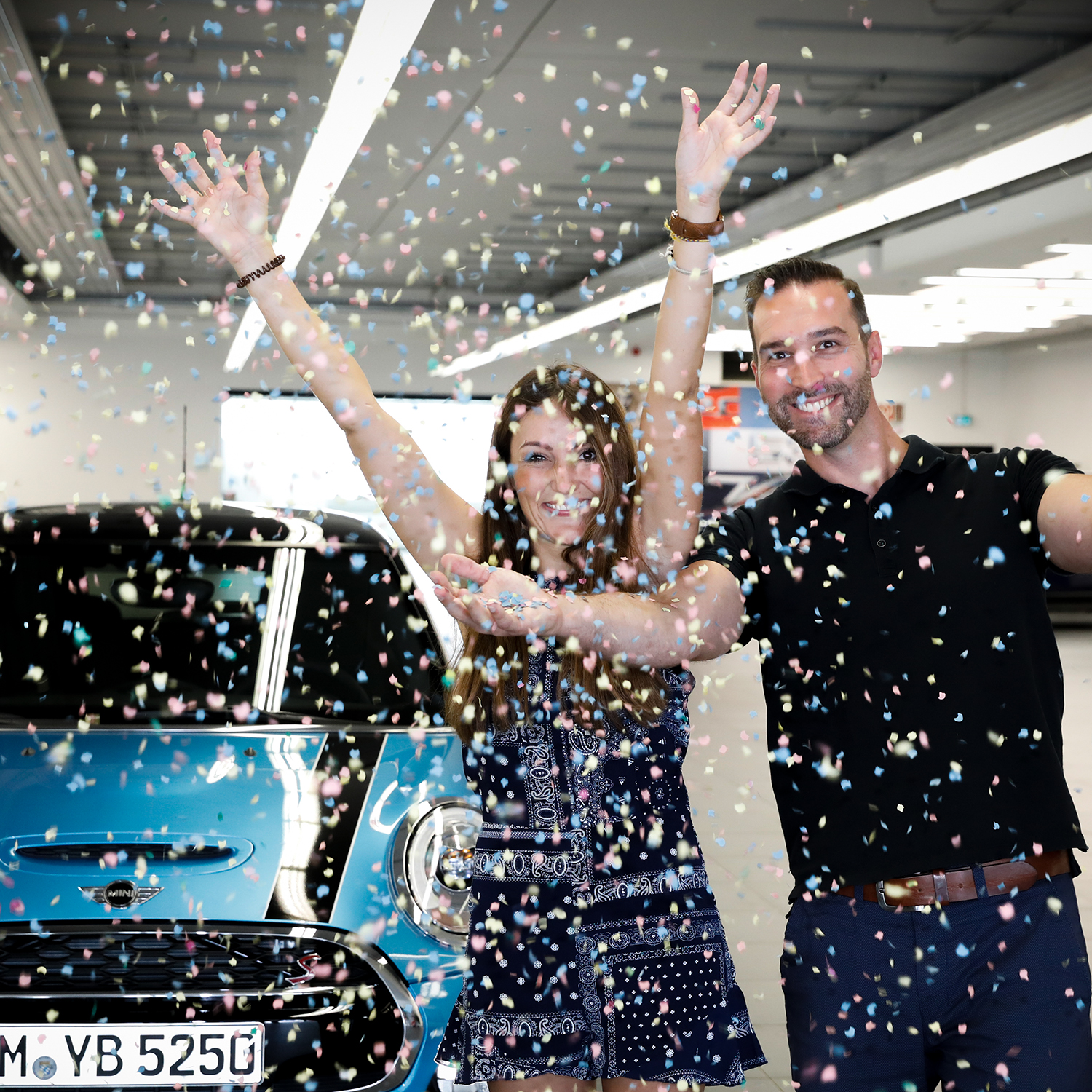 Une employée récupère sa nouvelle MINI et jette des confettis en l'air avec le vendeur.