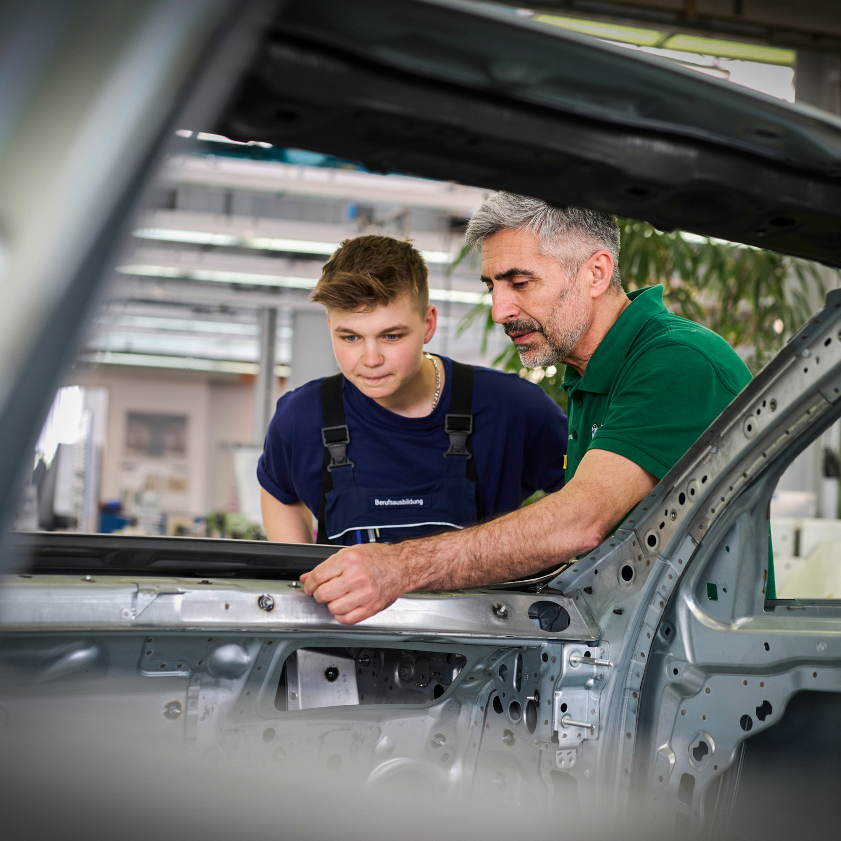 An apprentice and a supervisor working on a car body.