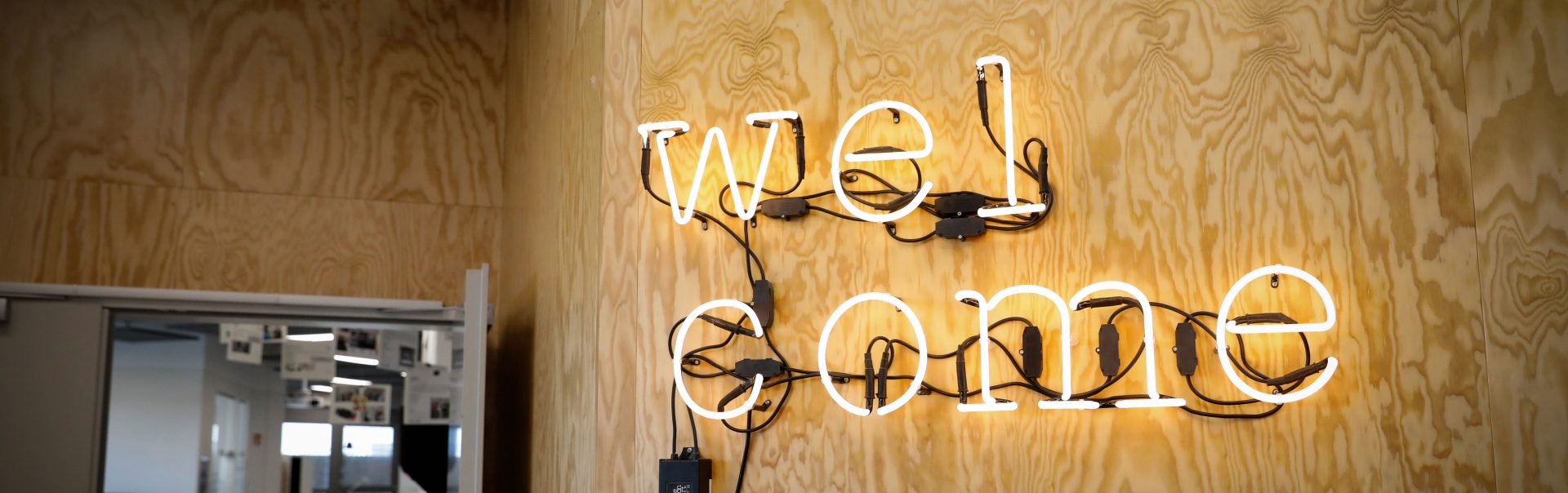 A neon welcome sign hanging on a wooden wall