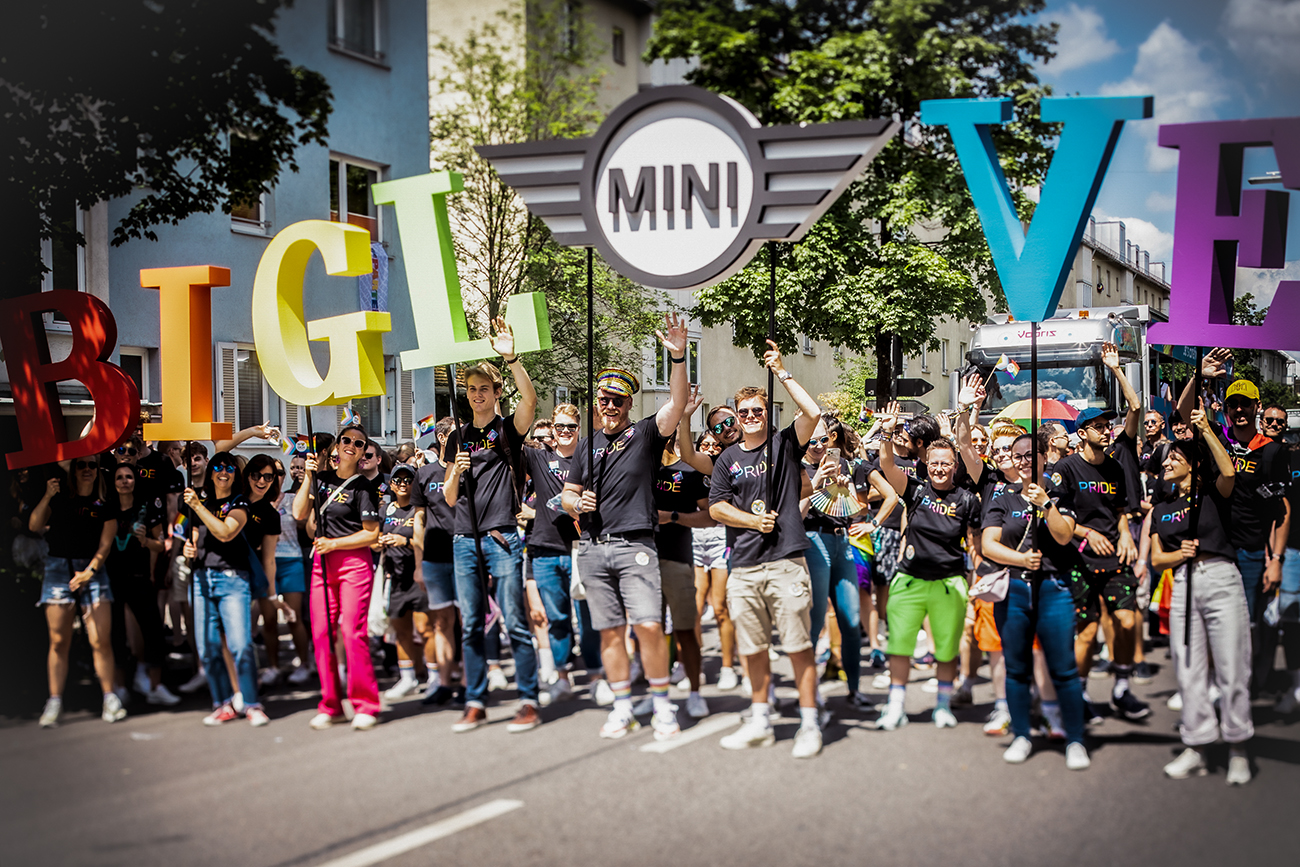 A Group of BMW Group employees holding up letters with the MINI slogan "Big Love" in rainbow colors.