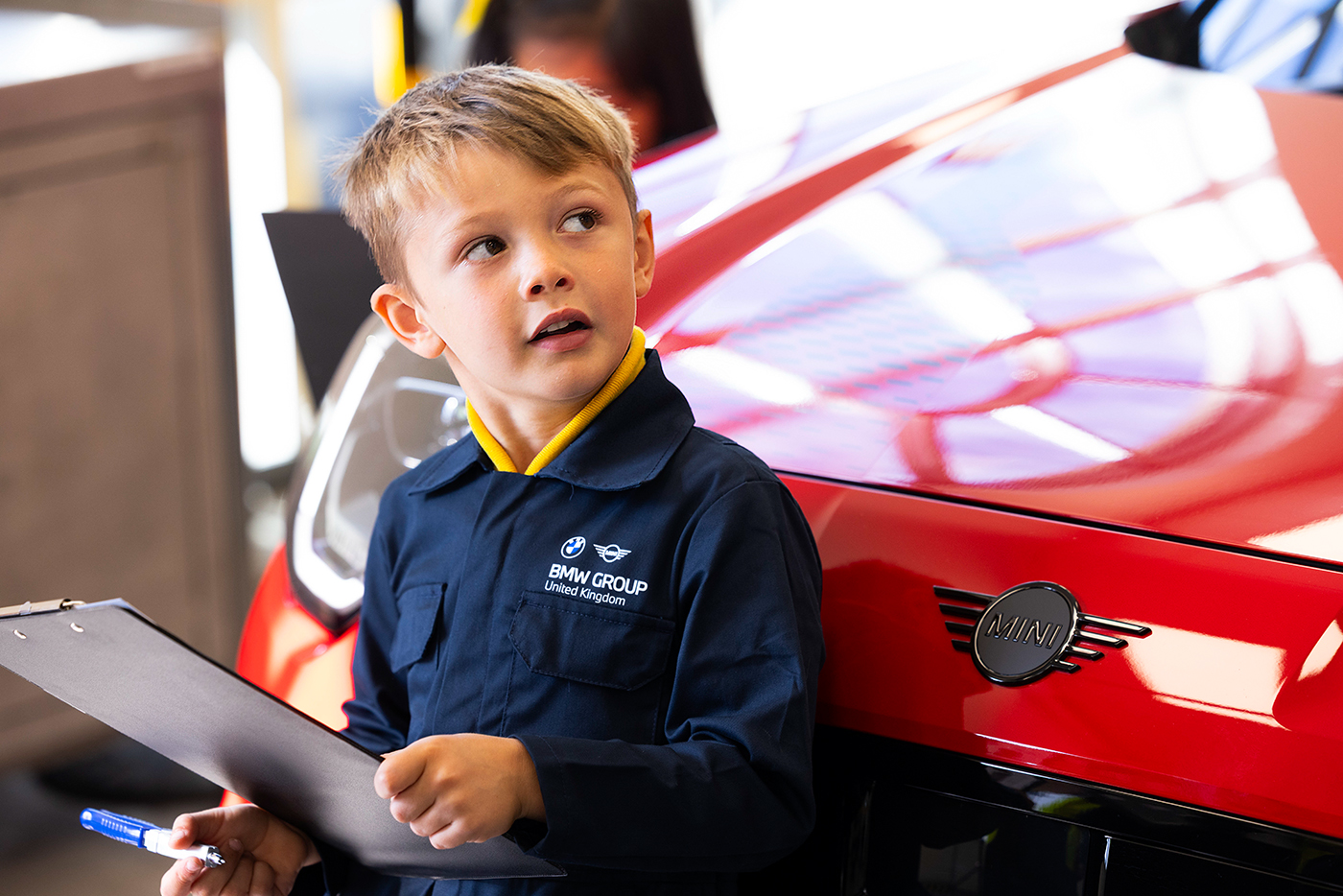 School student holding a clipboard next to a red BMW vehicle during a hands-on workshop at BMW Group.