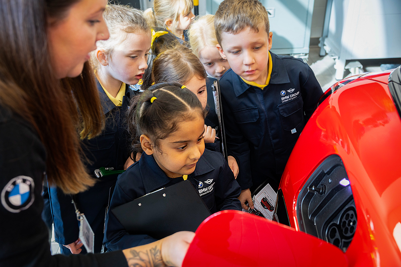 School students exploring the front section of a BMW vehicle during a workshop visit.