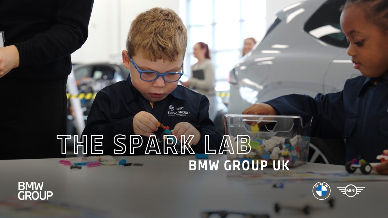 School students taking part in a hands-on building activity during a BMW Group UK Spark Lab workshop, with BMW vehicles displayed in the background.