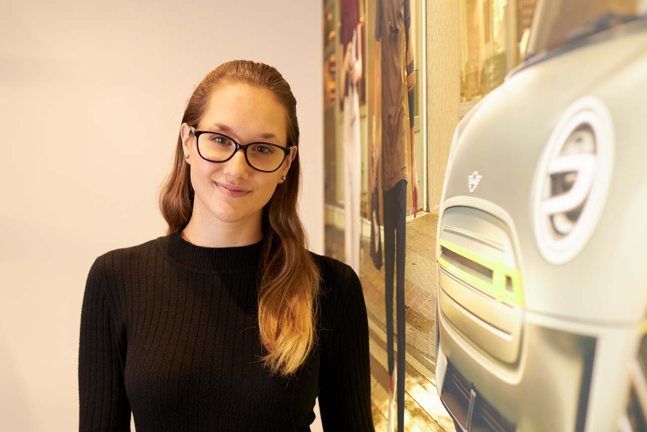 Ruby, a business apprentice standing next to a MINI wallpaper.
