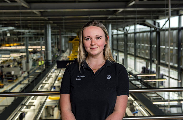 Louisa, a craft apprentice standing in a factory hall.