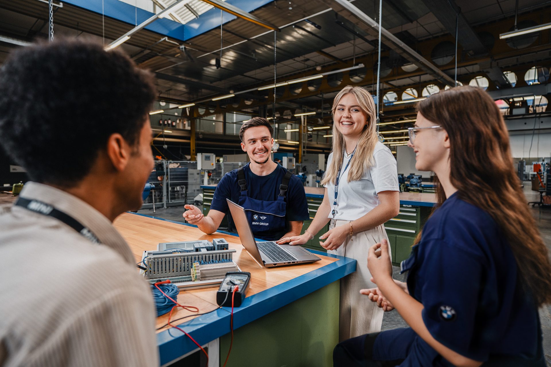 Four apprentices talking while standing at a work bench