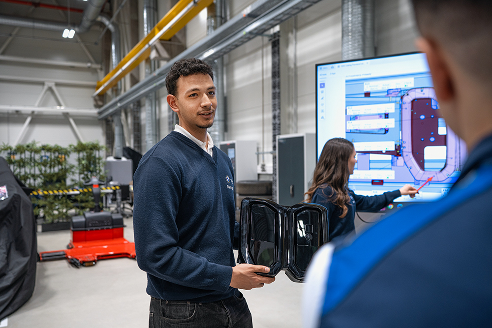 Employee presenting digital manufacturing information to colleagues on a production floor in an industrial facility.