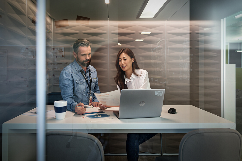 Employees reviewing financial data and working on a laptop in a glass meeting room.