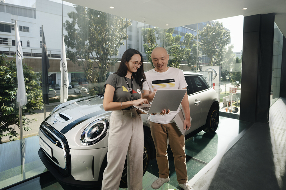 Employees reviewing product information on a tablet next to a vehicle showroom display.
