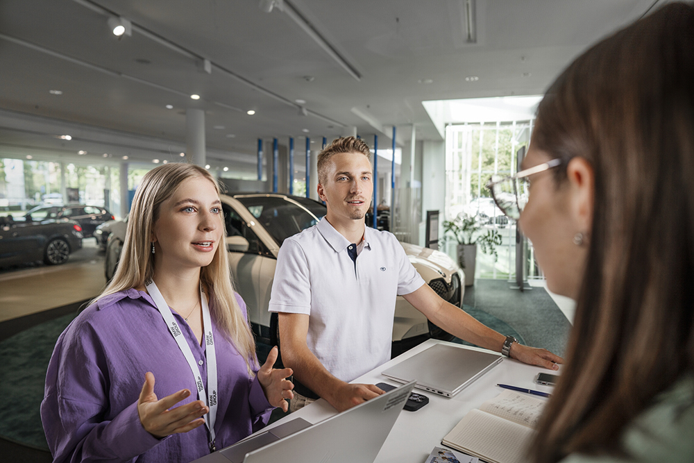 Team discussion in a modern showroom environment with vehicles displayed nearby.