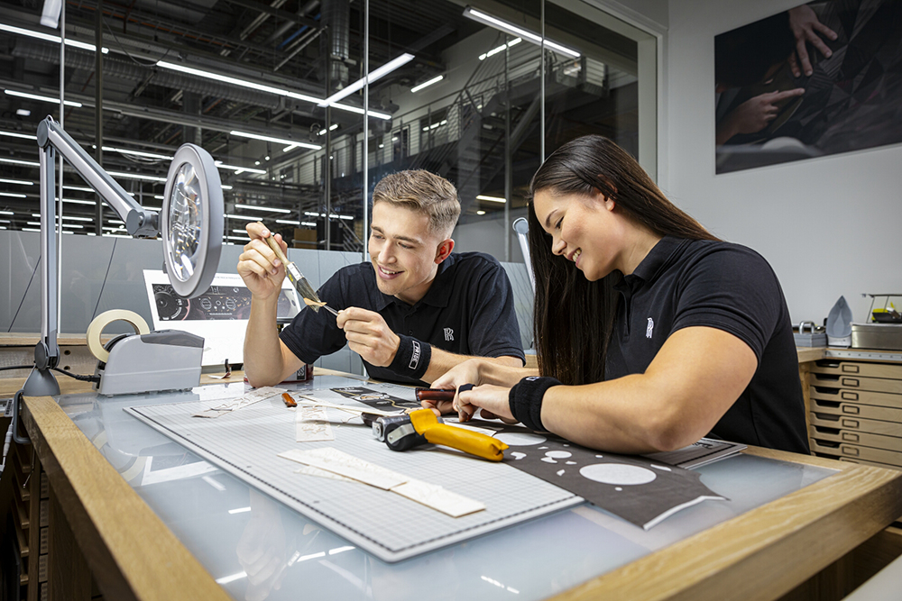 Employees working on a handcrafted automotive component at a workshop bench.