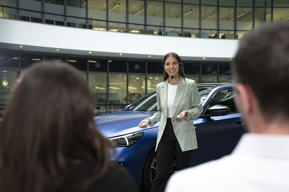 Employee presenting in front of a vehicle to an audience during a corporate event.