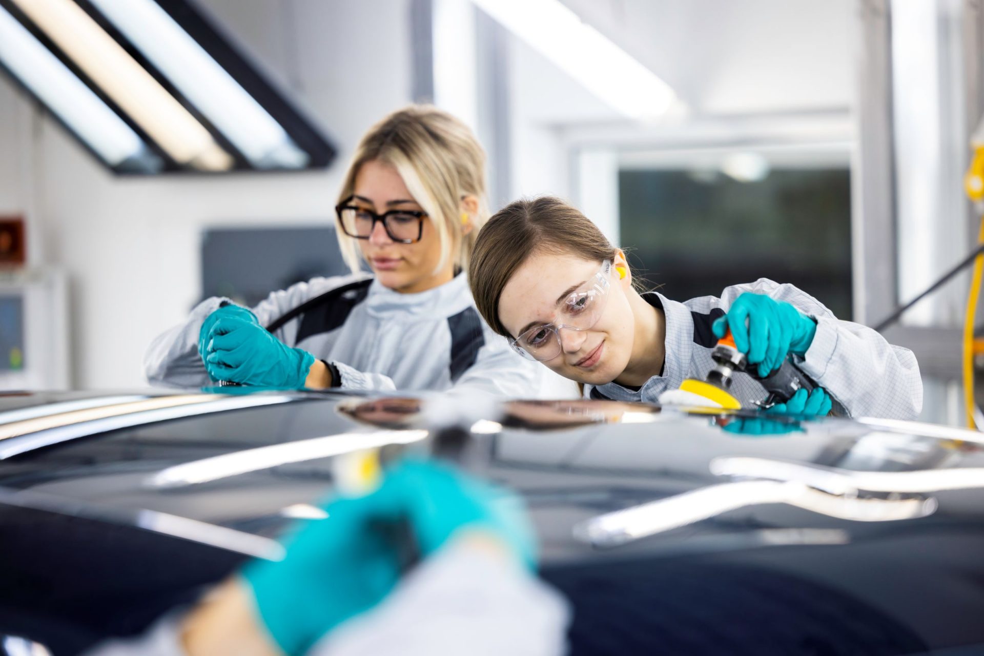 two BMW Group paint apprentices working on a car.
