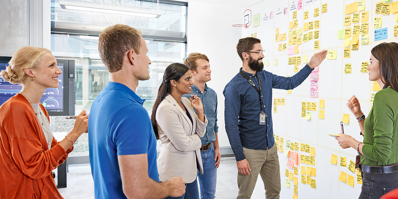 The picture shows a group meeting in front of a dashboard to represent communication jobs.
