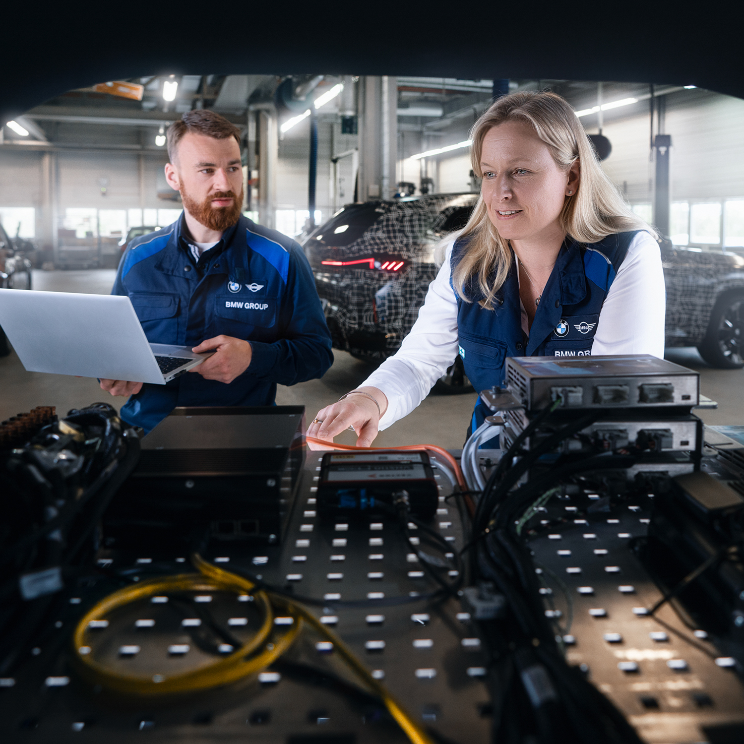 Two BMW Group engineers work on a technical device in the boot.