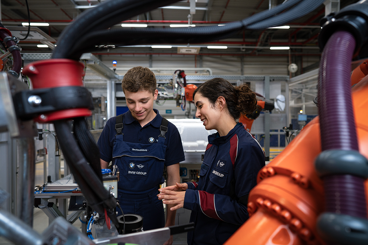 Two apprentices working with an industrial robot in production