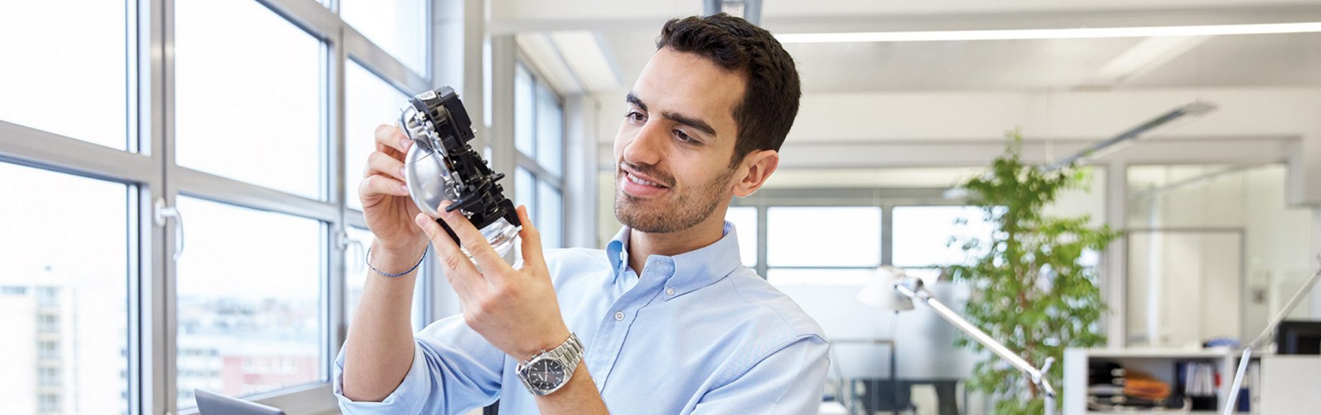 The picture shows a man in an office examining a car headlight.