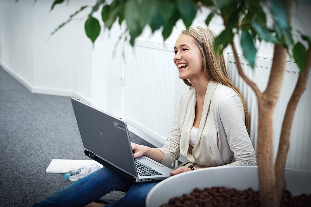 A BMW student is working with her laptop sitting on the floor