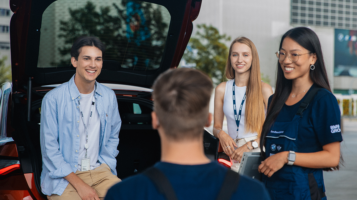 A group of four students having a conversation, one of them is sitting in the trunk of a car