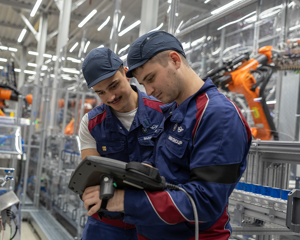Two BMW Group engineers work on a technical device in the boot.