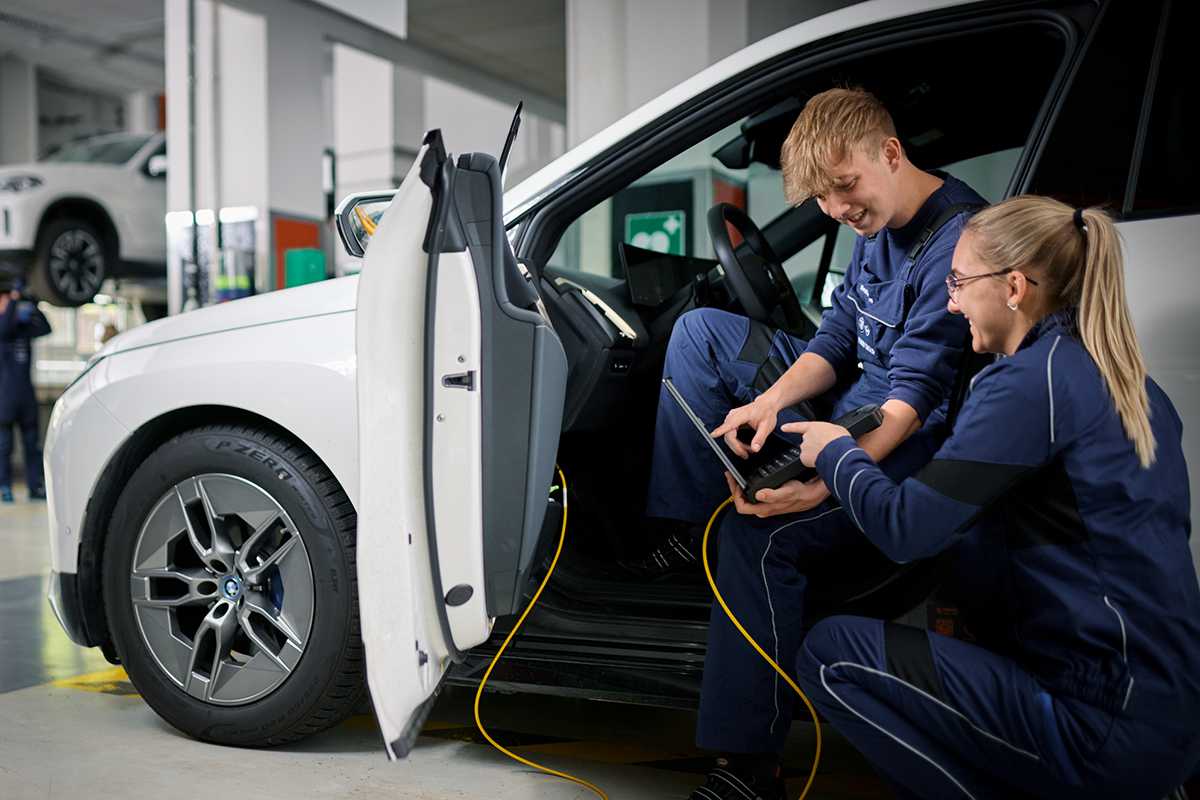 Két gyakornok egy elektromos BMW-n dolgozik egy elemző eszközzel.