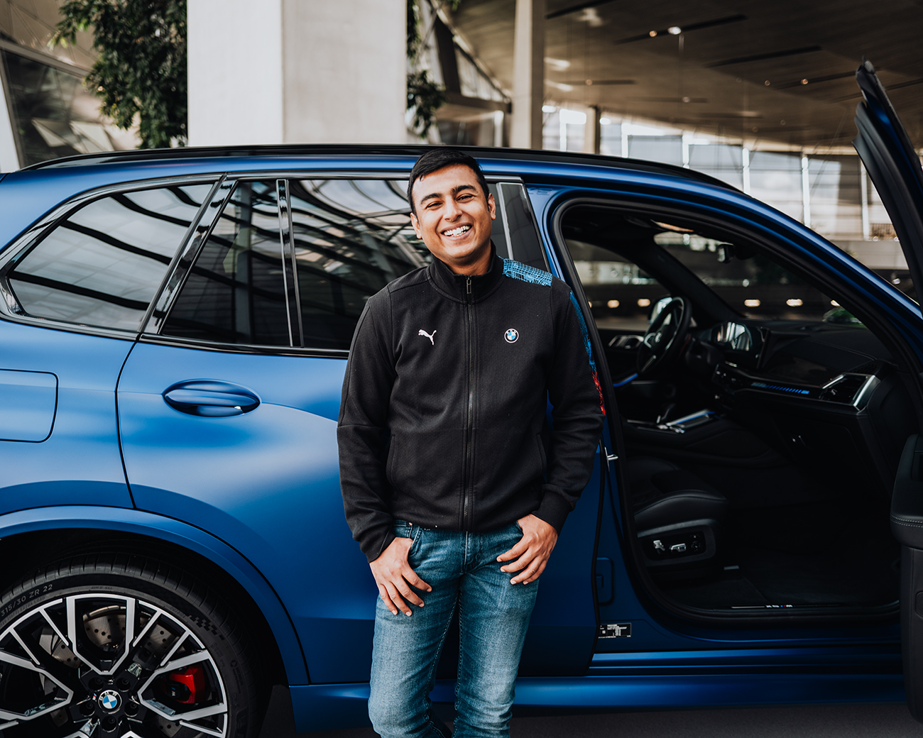 Kartikey laughs in front of a blue BMW X5M.