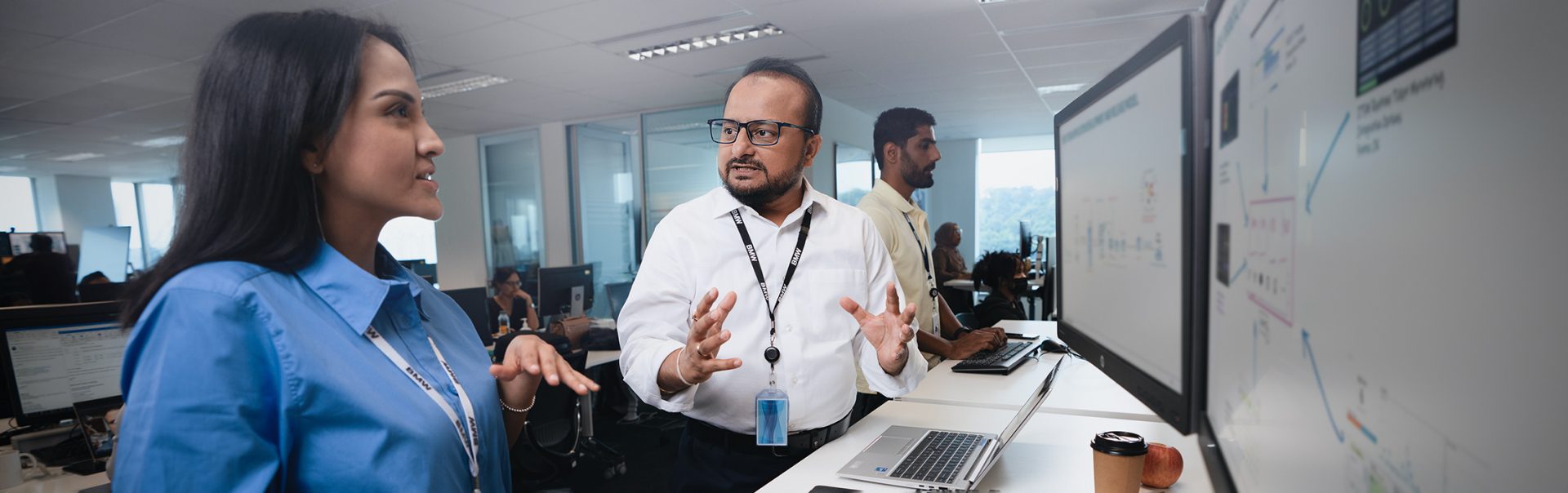 The photo shows a BMW IT employee talking to a colleague.