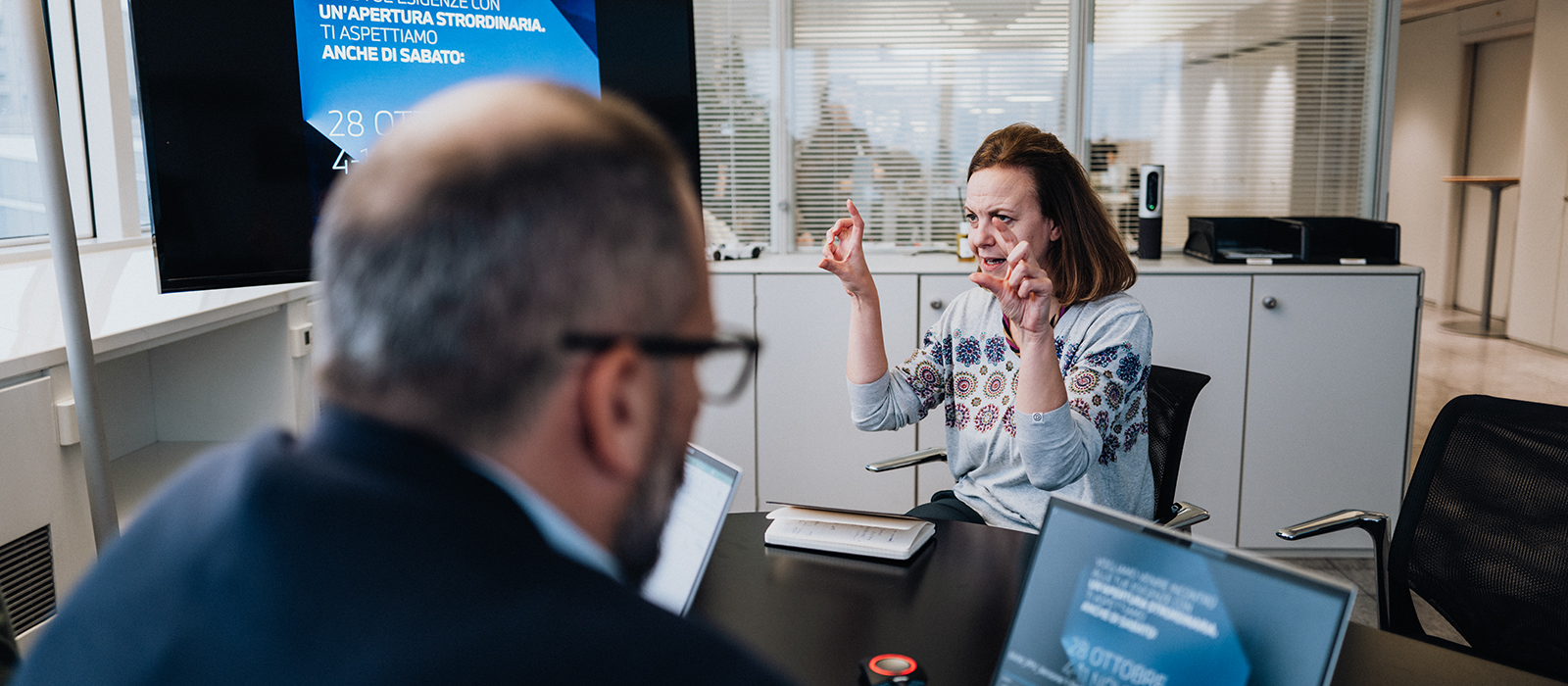 The picture shows a young man sitting in front of a laptop, inspecting a car part.