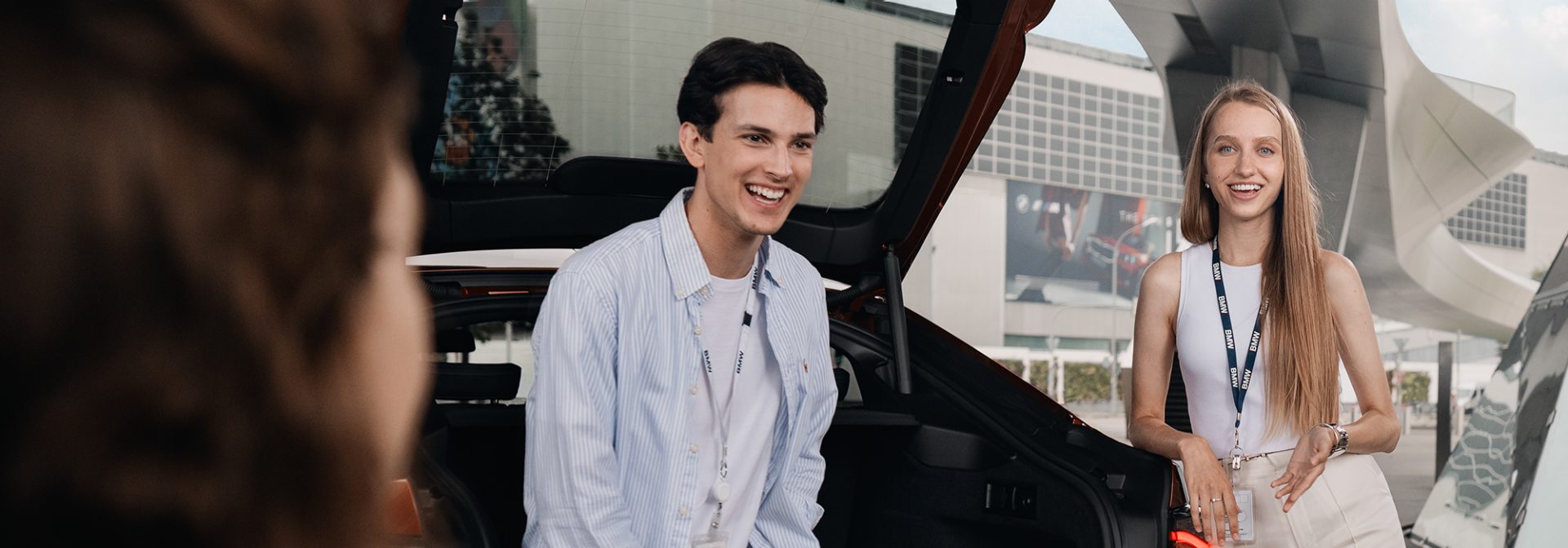 Three colleagues having a chat while two of them are sitting in the trunk of a car