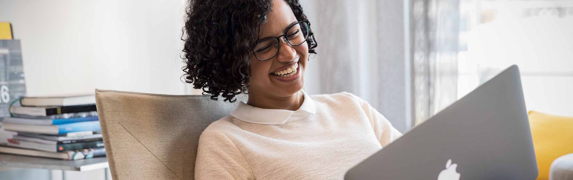 The picture shows a woman using her laptop and laughing.