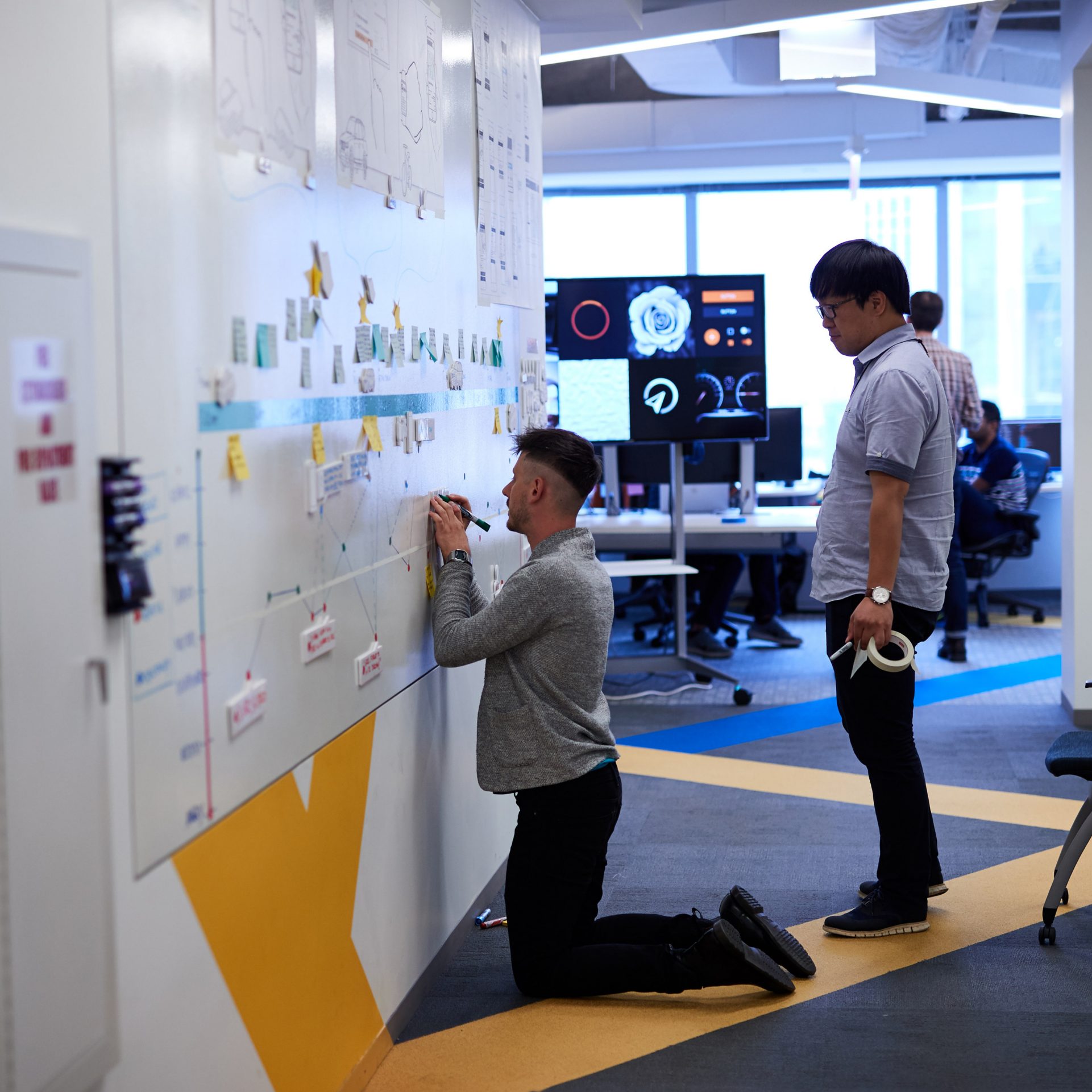 The picture shows two employees working at a project wall.
