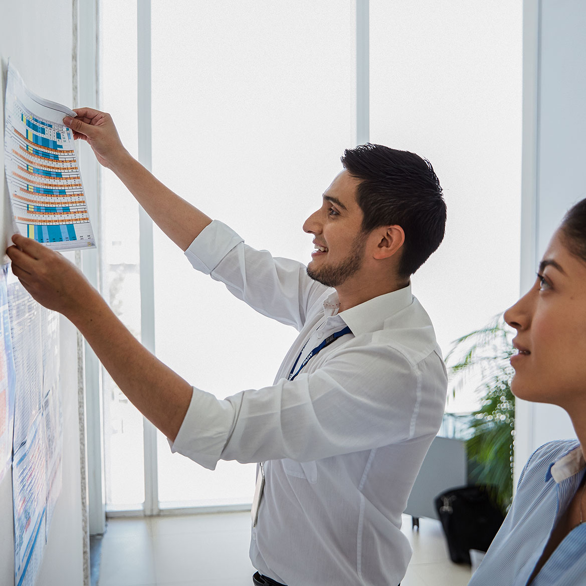 The picture shows two colleagues pinning notes on a wall.