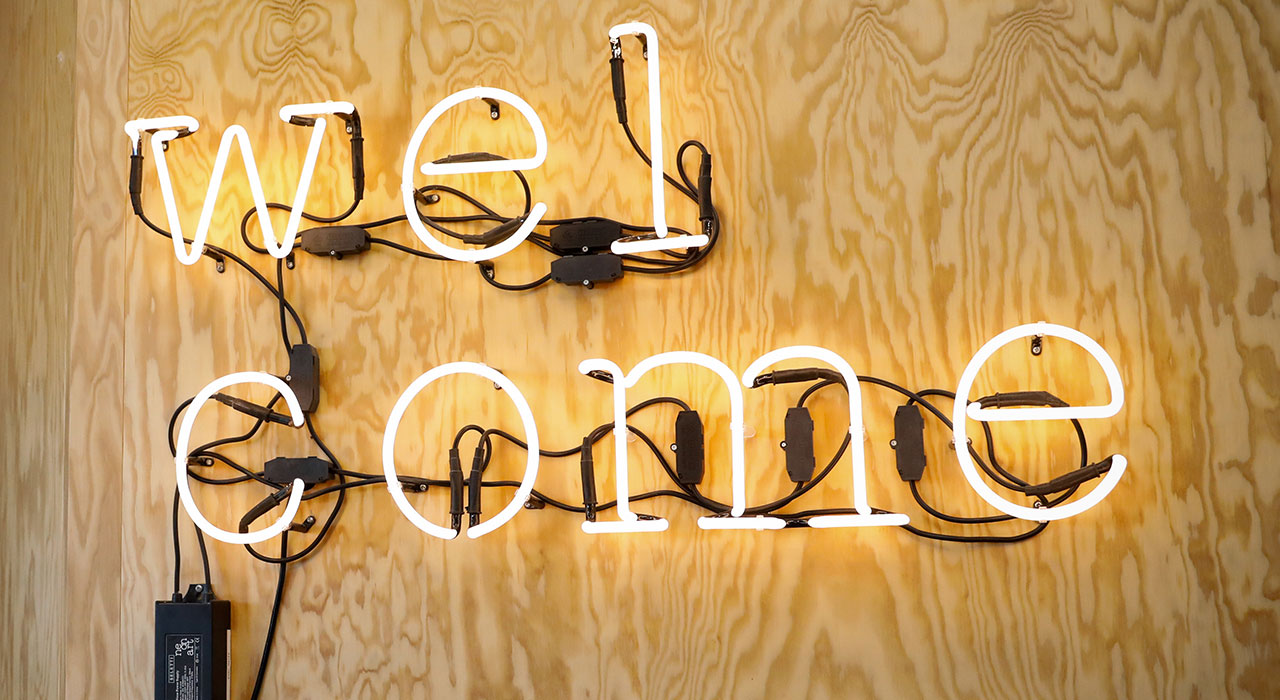 The picture shows the neon sign “welcome” hanging on a wall at the Innovation Lab in Munich.