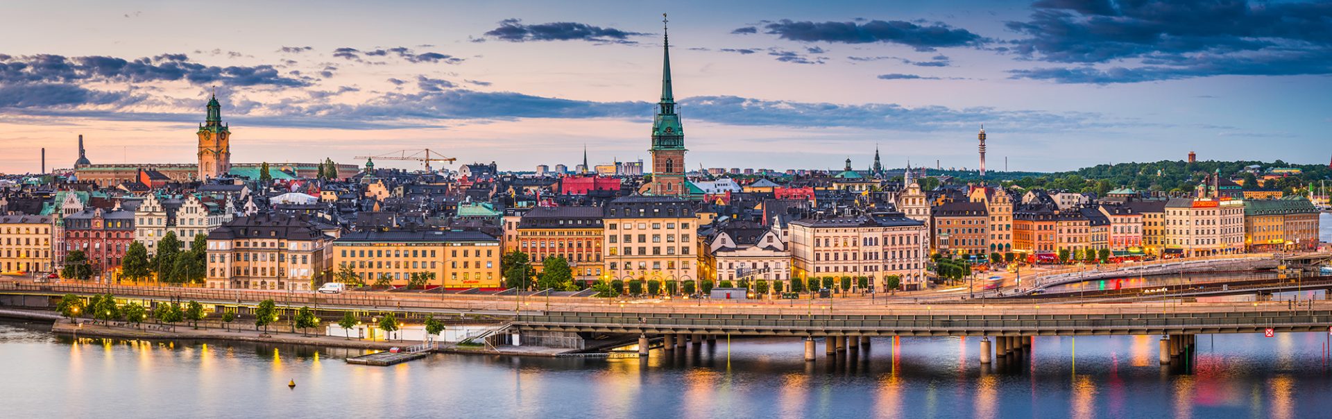 High angle panoramic view across the rooftops and spires of Gamla Stan as the dusk lights illuminate the heart of Stockholm, Sweden's vibrant capital city.