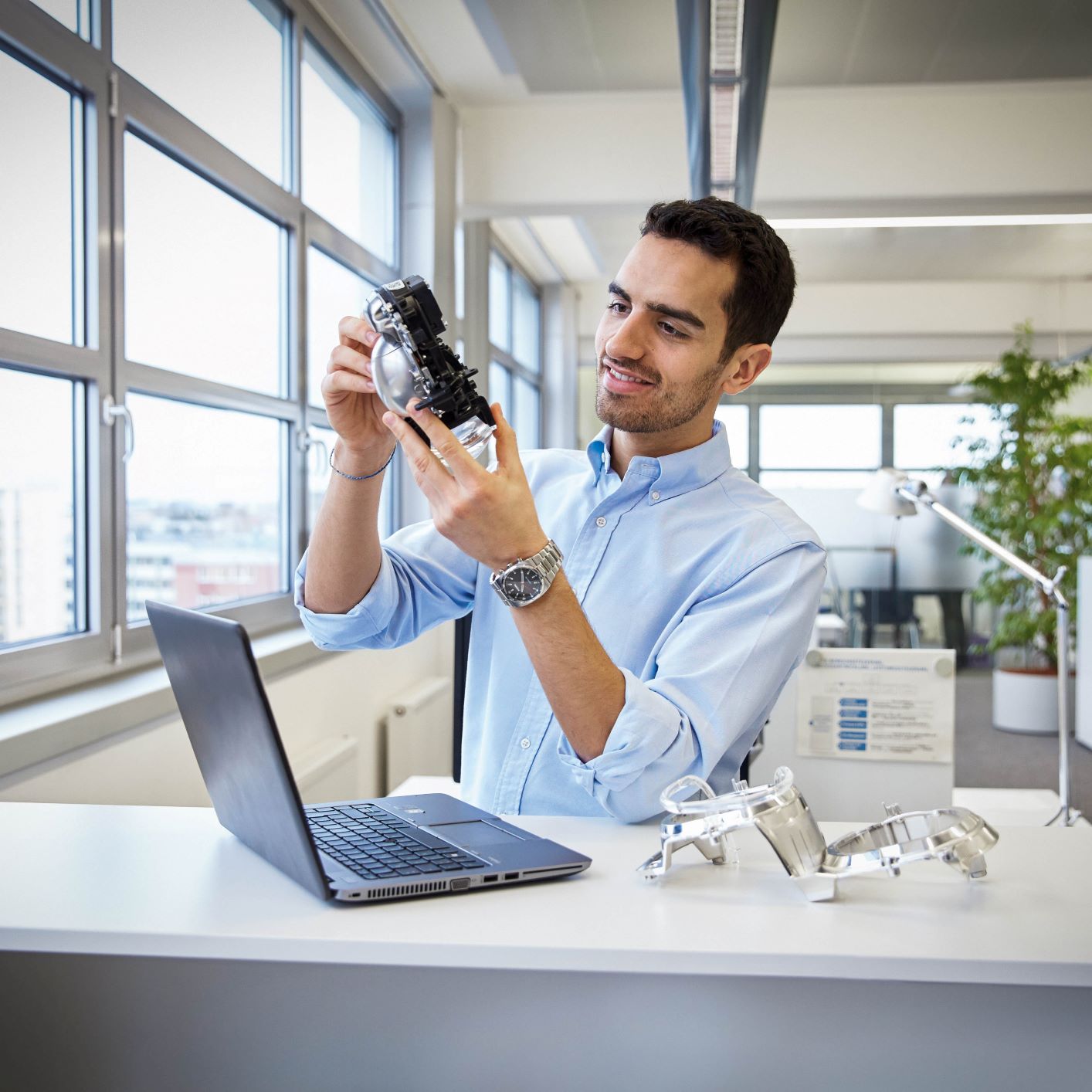 The picture shows a young man sitting in front of a laptop, inspecting a product.