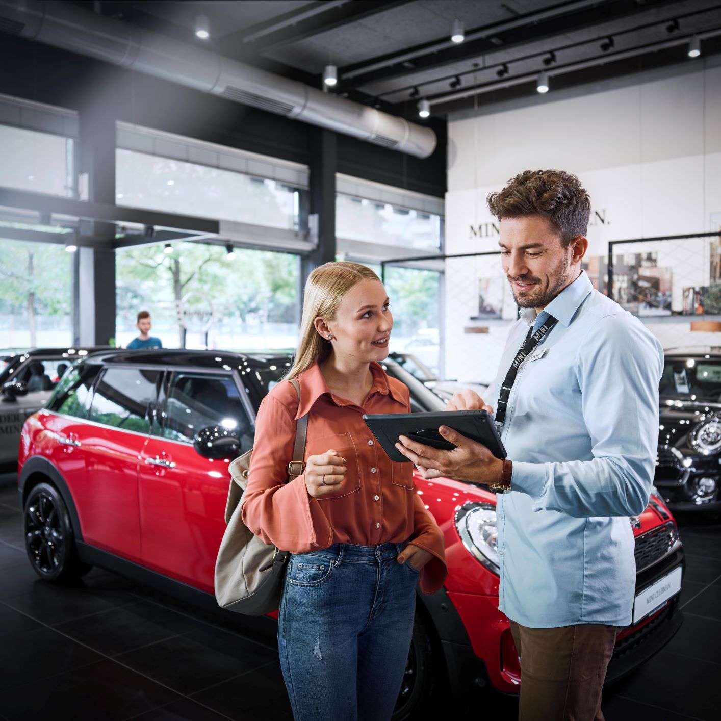 A BMW sales and distribution employee explains something to a customer on a tablet.