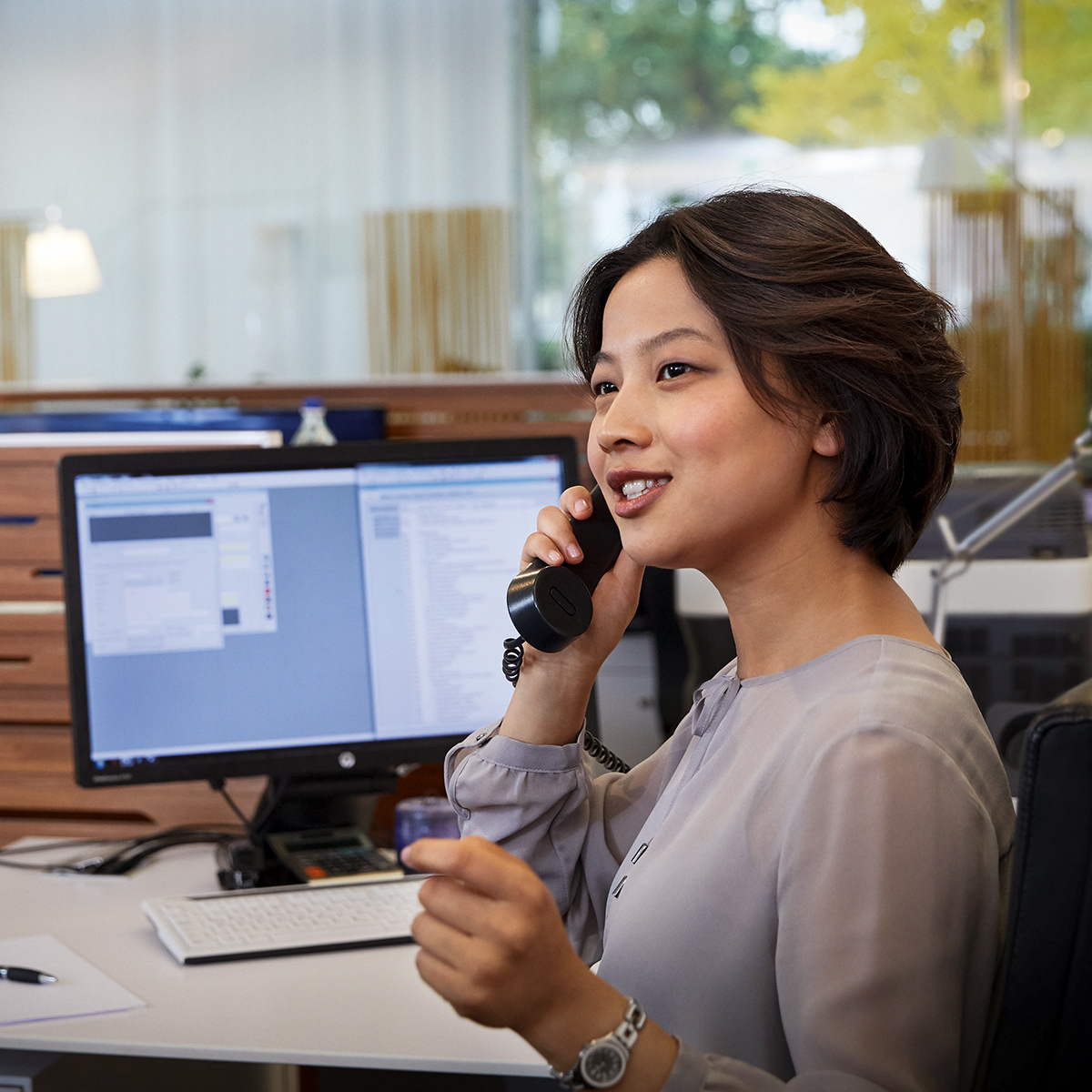 The picture shows a woman in an office, talking on the phone.