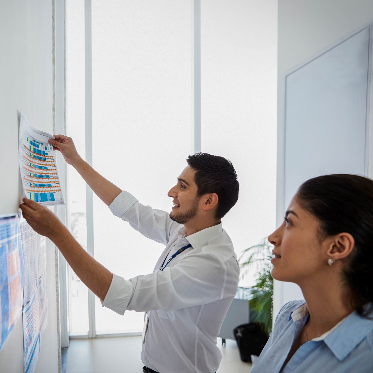 The picture shows to employees, a man and a woman, putting up posters on a wall.