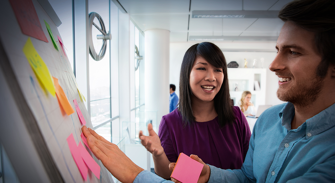 A woman and a man are sticking post-its to a wall.