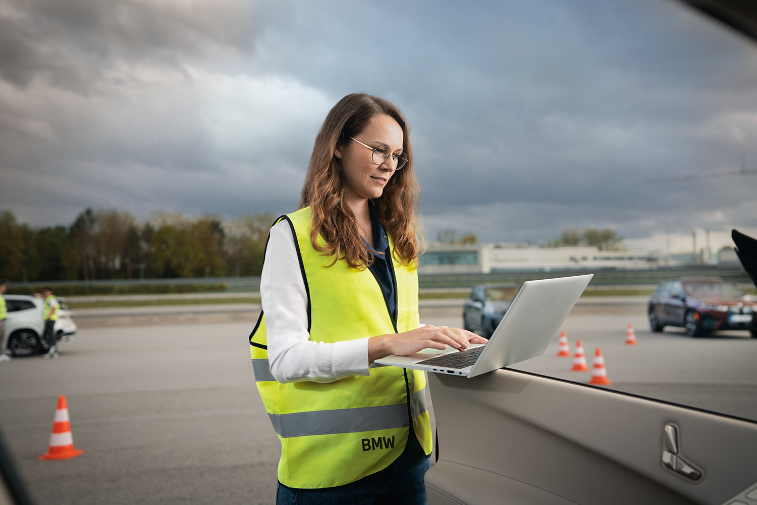 BMW engineer with a laptop on a vehicle door at a test site