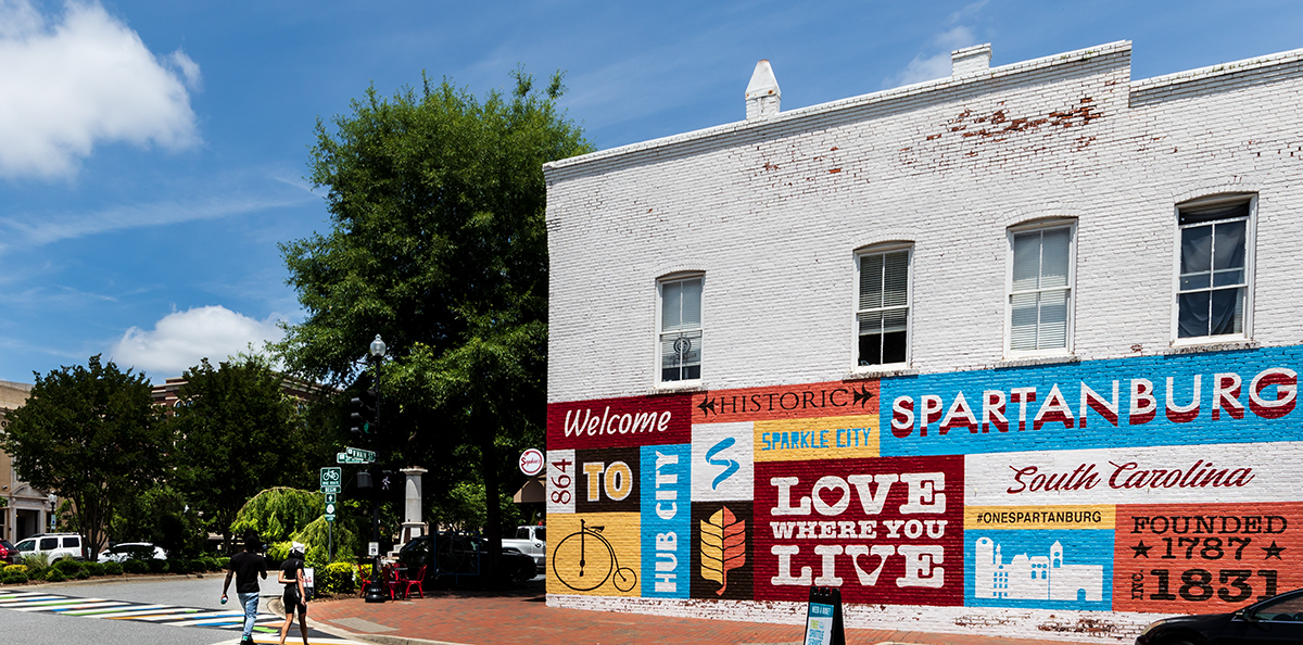 Spartanburg, SC, USA-13 June 2021: The heart of downtown, showing painted building welcome sign, Victorian building on the left of Boulevard, and a young couple walking.  Horizontal image.