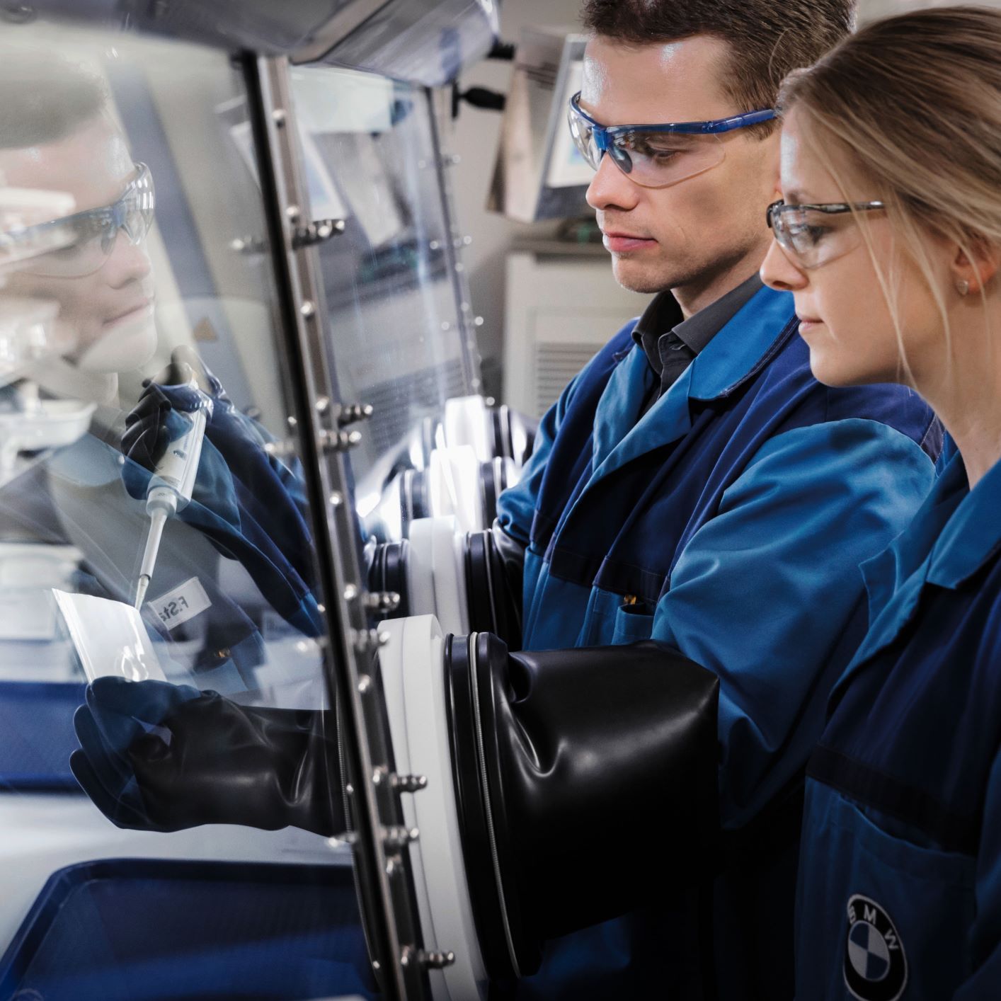 The image shows two BMW Group employees working in a lab.